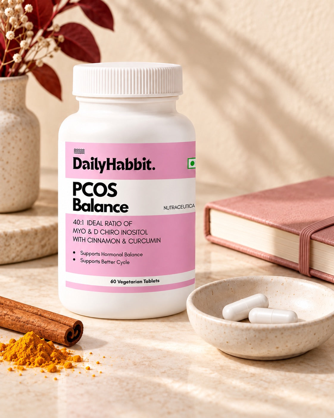 DailyHabbit PCOS Balance bottle, two white capsules and a journal with cinnamon and turmeric for an everyday routine.